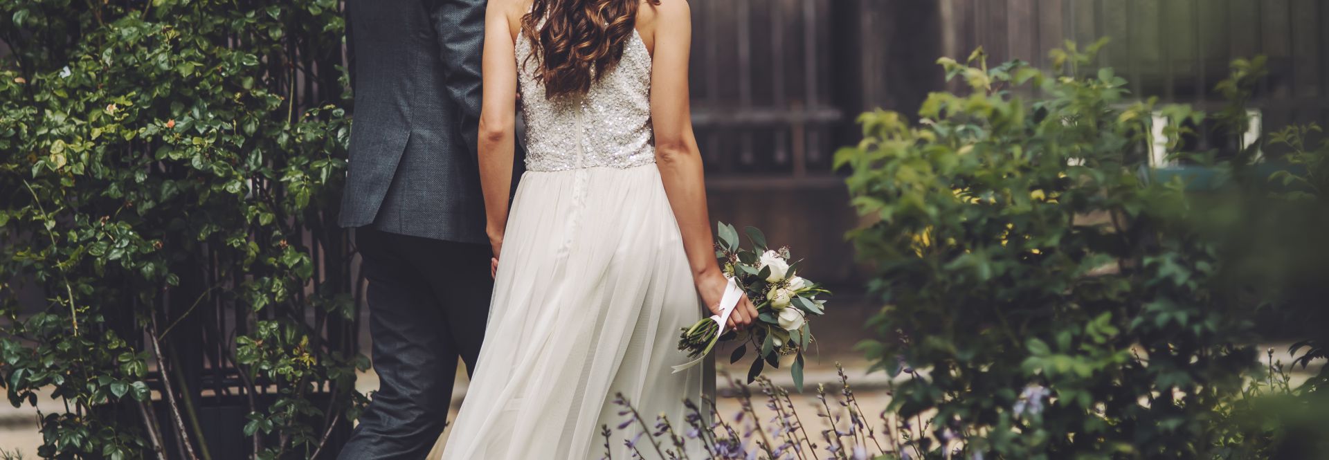 An image of a bride and groom holding hands walking through some greenery