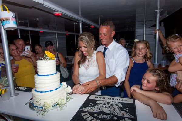 Wedding couple celebrates their wedding by cutting the cake during their sunset sailboat reception planned by Southernmost Weddings