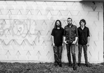 black and white image of three guys standing in front of a white wall